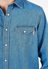 Camicia di jeans azzurro chiaro con colletto a punta, tasca frontale, bottoni bianchi e dettagli di cucitura arancione sui punti. Tessuto morbido, maniche lunghe.