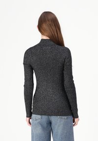 Svart, tettsittende genser med høy krage, ribbestruktur og metalltråder. Lange ermer og glatt finish, sammen med lyseblå jeans.