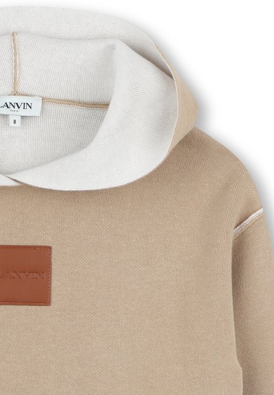 Felpa beige con cappuccio bianco. Presenta una toppa in pelle con logo e cuciture a contrasto. Texture morbida e design con vestibilità rilassata.