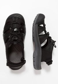Black outdoor sandal with synthetic upper, adjustable straps, and rubber sole. Features a textured insole and protective toe cap for durability.