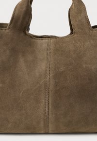 Brown suede handbag with double handles and visible vertical stitching in the center on a light background.