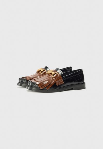 Black and brown loafers with decorative tassels and gold buckles, set against a clean white background.