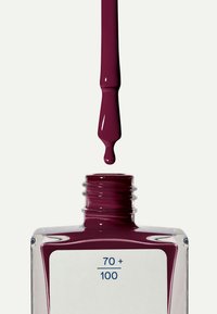 Smalto per unghie bordeaux in una bottiglia di vetro quadrata, con una superficie liscia e un'etichetta bianca che mostra i numeri 70 + 100. Applicatore gocciolante.