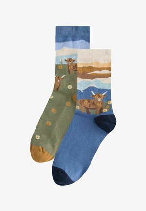 Gestrickte Socken mit einem Farbdesign in Grün und Blau, Mustern von Kühen und Blumen, kontrastierenden gerippten Bündchen und durchgefärbten Zehen.