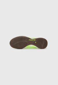 Flat brown sole of neon yellow Adidas Predator indoor soccer shoe with textured grip and logo.