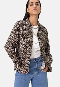 Leopard print shirt in soft fabric, long sleeves, collared design, paired with a white top and high-waisted blue jeans. Gold jewelry accents.
