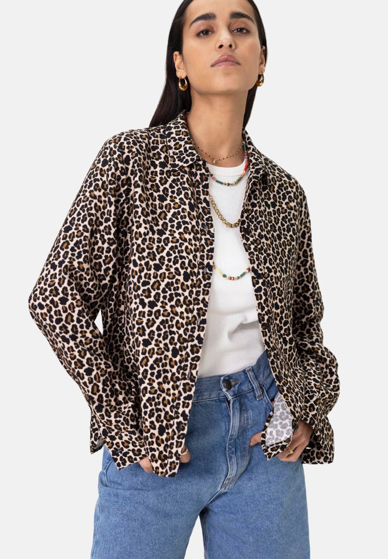 Leopard print shirt in soft fabric, long sleeves, collared design, paired with a white top and high-waisted blue jeans. Gold jewelry accents.