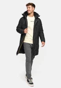 Zwarte donzen jas met een capuchon, ritssluiting aan de voorkant en zijzakken. Draag over een licht crèmekleurig sweatshirt en grijze broek, gecombineerd met sportschoenen.