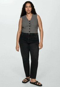 Siv obarvan brezrokavnik s šestimi črnimi gumbi, v kombinaciji s črnimi visokim pasom in črnimi sandalami. Preprost, oprijet dizajn.