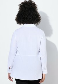 Weißes Langarmhemd mit strukturiertem Stoff, abgerundetem Saum und Knopfmanschetten. Die Rückansicht zeigt eine taillierte Form mit einem Kragen.