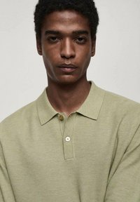 Light green polo shirt made of textured fabric, featuring a collar, two-button placket, and short sleeves. Plain design without patterns.