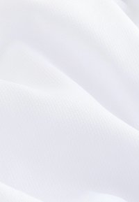 Gros plan d’un tissu blanc lisse avec un motif texturé subtil et des plis doux créant des ombres délicates.