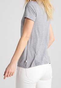 T-shirt grigio in cotone con maniche corte, vestibilità comoda e orlo arrotondato; abbinato a jeans bianchi, presenta un look informale.