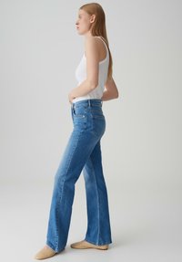 Blauwe high-waisted flare jeans van denim met een zachte textuur, met traditionele zakken en een lichte wassing, gecombineerd met een witte tanktop.