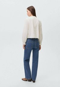 Blusa di crema tagliata con maniche a sbuffo, abbinata a jeans blu a vita alta e stivali alla caviglia marroni. Design semplice, texture morbida.