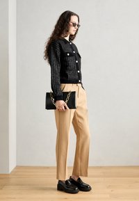 Čierny pletený kardigán so zlatými gombíkmi, béžové tailored nohavice, čierne kožené mokasíny a čierna kabelka s zlatým reťazcom.