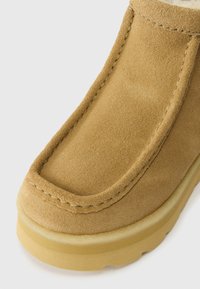 Smeđe nubuk gležnjače s okruglim vrhom, šavnim detaljima i gumeni potplat, s mekim, teksturiranim gornjištem i minimalnim akcentima.