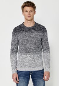 Grijs en marineblauwe gradient trui met lange mouwen, ronde hals en een gestructureerd breipatroon, gecombineerd met blauwe jeans. Voorzien van geribbelde manchetten.