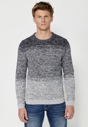 Pulover gradient gri și bleumarin cu mâneci lungi, guler rotund și model de tricot texturat, asortat cu blugi albaștri. Dispune de manșete cu torsade.