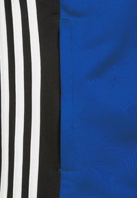 Blauer Stoff mit glatter Textur, angrenzend an ein schwarzes Paneel mit drei weißen Streifen. Das Design umfasst präzise Nähdetails.