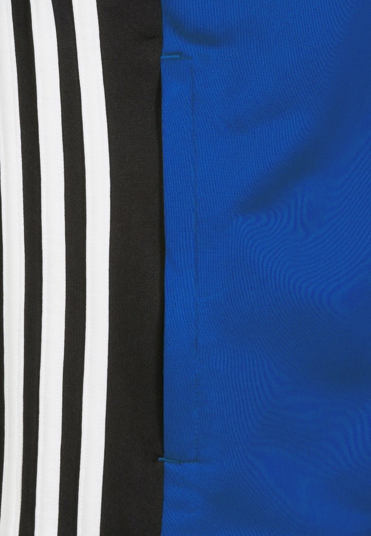 Blauer Stoff mit glatter Textur, angrenzend an ein schwarzes Paneel mit drei weißen Streifen. Das Design umfasst präzise Nähdetails.