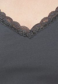 Κοντινό πλάνο ενός γκρι ντεκολτέ ρούχου με μαύρη δαντέλα σε ανοιχτόχρωμο δέρμα.