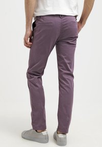 Fioletowe bawełniane spodnie o slim fit, z gładką fakturą, tylnymi kieszeniami i casualowym wyglądem, zestawione z jasnoszarymi sneakersami.