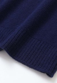 Gros plan d’un tissu tricoté bleu foncé avec un ourlet côtelé, montrant un matériau doux et texturé en laine ou en fil.