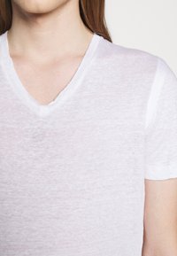 Bílá, krátkosleeve V-krční tričko z lehkého, mírně průsvitného materiálu, s uvolněným střihem a hladkou texturou.