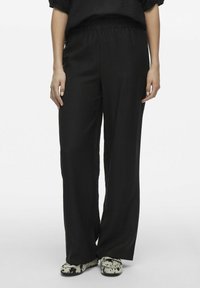 Melni platā kāju bikses ar teksturētu audumu, ar elastīgu jostu un brīvu piegriezumu. Akcentētas ar rakstainām kurpēm.