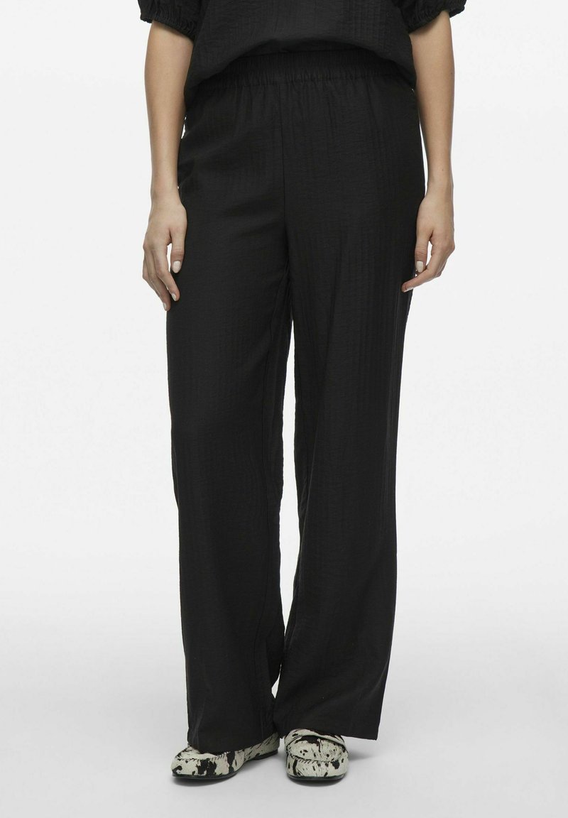 Melni platā kāju bikses ar teksturētu audumu, ar elastīgu jostu un brīvu piegriezumu. Akcentētas ar rakstainām kurpēm.