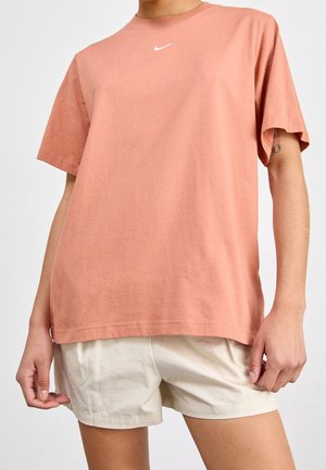 T-shirt en coton orange à manches courtes et col rond, avec un petit logo Nike blanc sur la poitrine. Associé à un short beige clair.