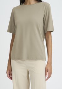 Lysebrun t-shirt med korte ærmer lavet af blødt stof med rund halsudskæring og afslappet pasform, kombineret med beige bukser med brede ben.