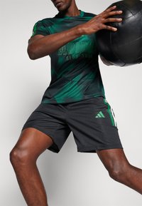 Adidas sportswear featuring a green and black patterned shirt and black shorts with green and white striped accents, designed for athletic performance.