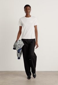 T-shirt bianca in cotone con un piccolo logo sul petto, abbinata a pantaloni neri larghi e con una giacca blu a fantasia floreale. Scarpe col tacco nere.