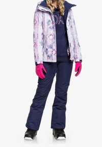 Zimní bunda s barevným geometrickým vzorem, spárovaná s námořnickými kalhotami. Růžové rukavice a černé sněhové boty dotvářejí outfit.