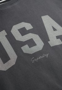 Donkergrijze sweatshirt met grote, reflecterende "USA" letters en het "Superdry" logo in kleinere tekst. Gemaakt van een katoenmix, met een ronde hals ontwerp.