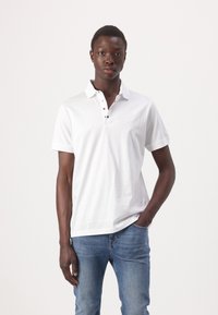 Witte polo met korte mouwen, met een kraag en zwarte knoopdetails. Gecombineerd met blauwe slim-fit jeans.
