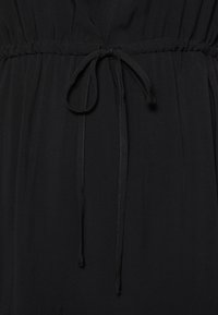 Svart klänning med insvängd midja och dragsko. Tyget verkar mjukt med en subtil glans och slät textur.