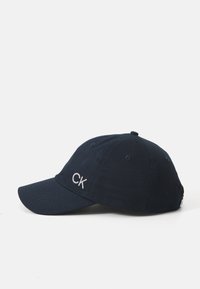 Sötétkék pamut baseball sapka ívelt karimával, fehér hímzett "CK" logóval, hat szellőzőlyukkal és állítható hátsó pánttal.