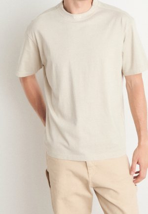 T-shirt beige clair à col rond, fabriqué en coton doux, avec des manches courtes et une coupe relaxée. Présente un logo subtil au niveau de l'encolure.