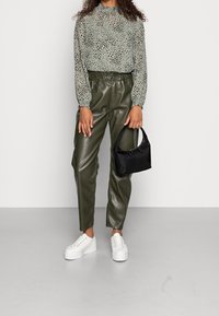 Blusa verde con estampado de animales y mangas largas, combinada con pantalones de imitación de cuero oliva de tiro alto y zapatillas blancas de plataforma. Bolso negro.