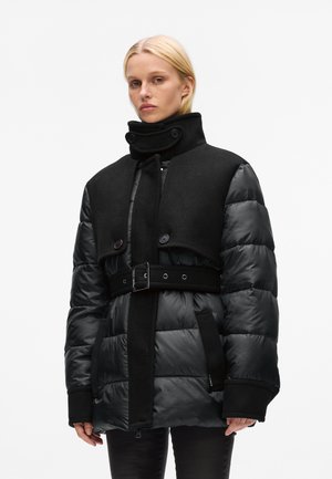 Black puffer jacket with a high collar and double-breasted button closure. Features a belted waist and contrasting wool and quilted textures.