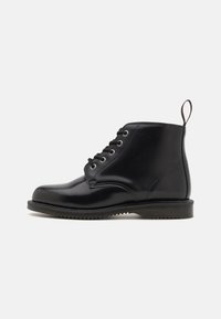Botas negras de cuero hasta el tobillo con punta redonda, que cuentan con seis ojales, cordones planos, un tacón bajo y una lengüeta en la parte trasera.