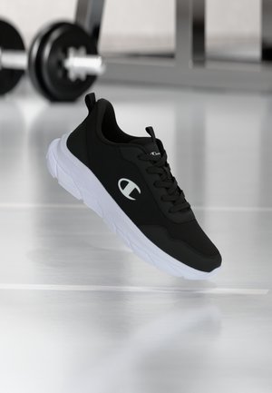 Melns sporta apavu ar baltu zolīti un logotipu, peldošs virs sporta zāles grīdas, fonā izplūdušas hanteles.