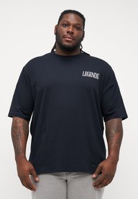 Black cotton t-shirt with short sleeves, featuring white "LEGENDS" text on the upper left chest. The fabric appears smooth and untextured.