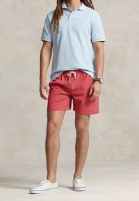 Ljusblå pikétröja, röda badshorts med snörning och vita sneakers. Inkluderar logoprydnader på tröjan och shortsen.