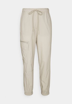 Hellbeige Cargo-Hosen mit elastischem Bund, Kordelzug, seitlicher Reißverschlusstasche und elastischen Bündchen, dargestellt vor einem schlichten weißen Hintergrund.