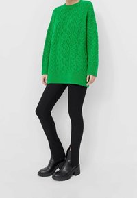 Pull vert en maille torsadée oversize avec col rond, assorti à un pantalon noir ajusté et des bottines noires épaisses avec des fentes latérales.