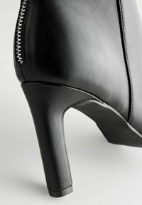 Stivaletto nero con tacco alto in pelle liscia, dotato di cerniera laterale e tacco affusolato, progettato per una silhouette aderente.